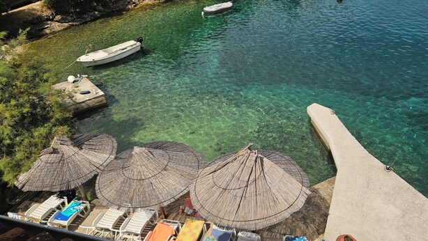 A clear view of a beach with boats, umbrellas, and lounge chairs.