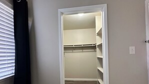 Een smalle inloopkast met planken en een deur naar een kamer.