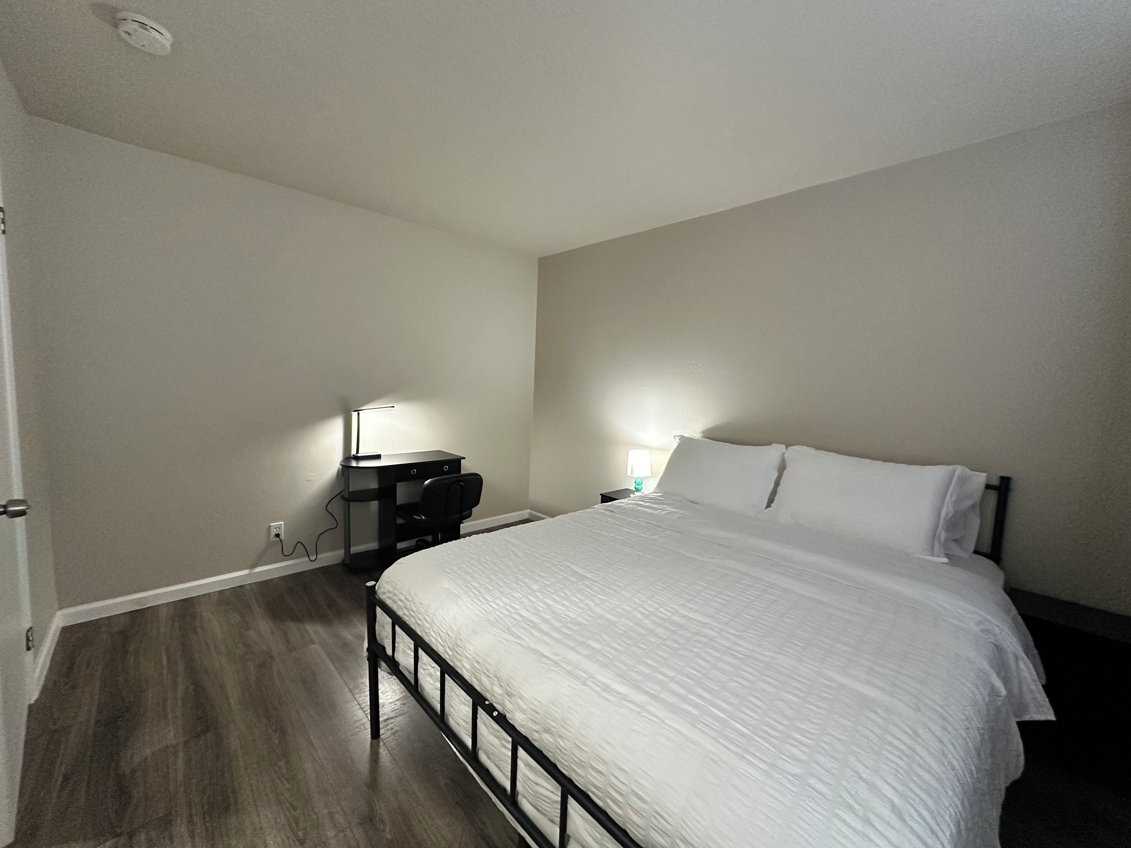 Un dormitorio con cama, escritorio, silla, lámpara y mesita de noche.