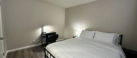 Un dormitorio con cama, escritorio, silla, lámpara y mesita de noche.