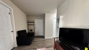 Een woonkamer met een zwarte bank, een televisie op een houten dressoir en een kamerbreed tapijt.