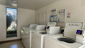 Een wasserette met vier voorladers, wasmachines en drogers, een raam met uitzicht en een rookverbods bord aan de muur.