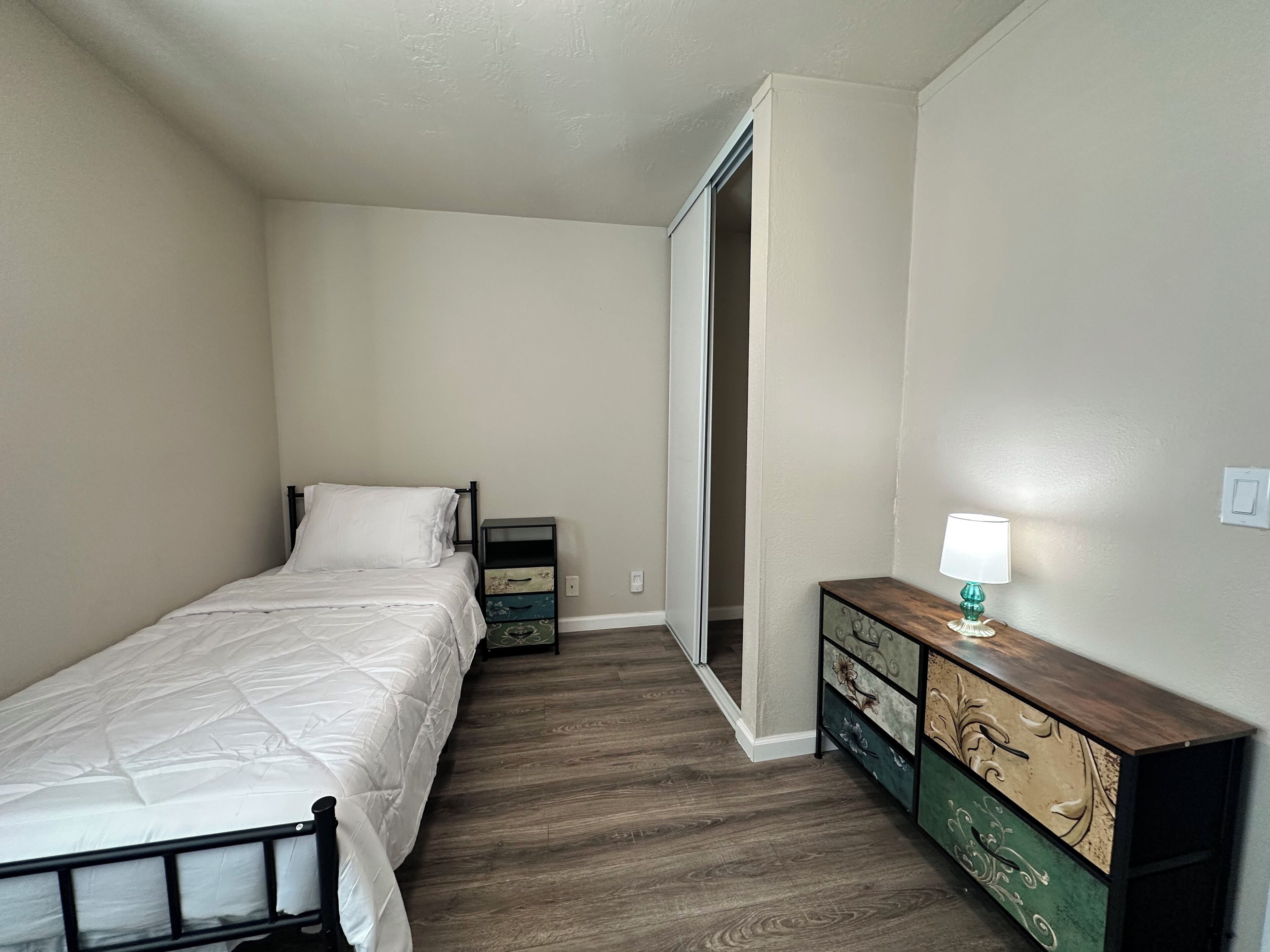 Une chambre à coucher comprenant un lit, une table de chevet, une commode et une porte donnant sur une autre pièce.