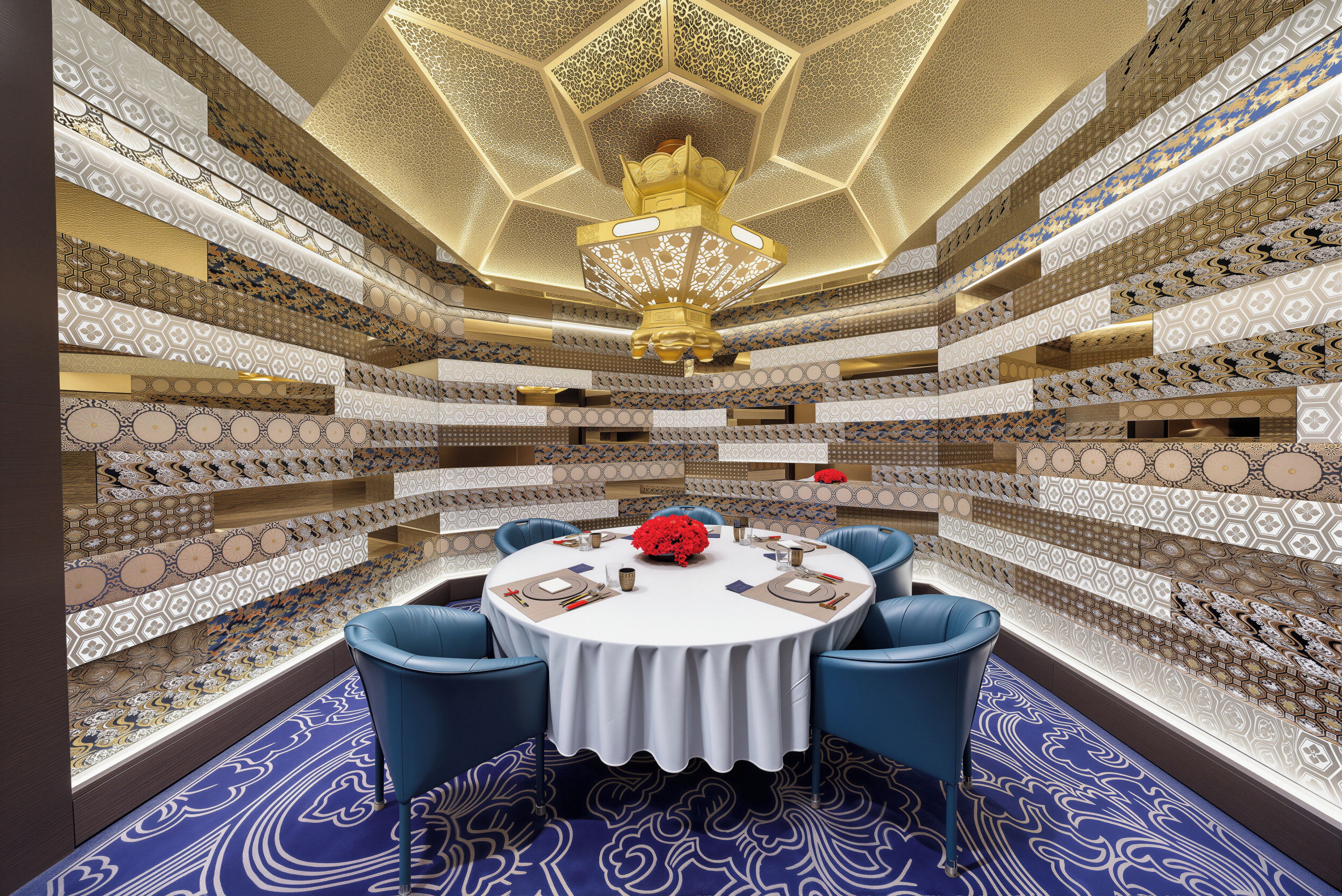 A circular table with blue chairs, surrounded by patterned walls and a chandelier.