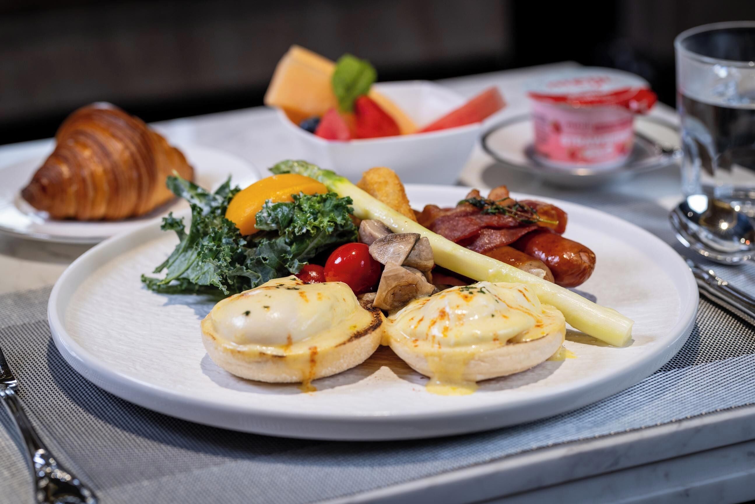A breakfast plate with eggs benedict, vegetables, and a croissant.