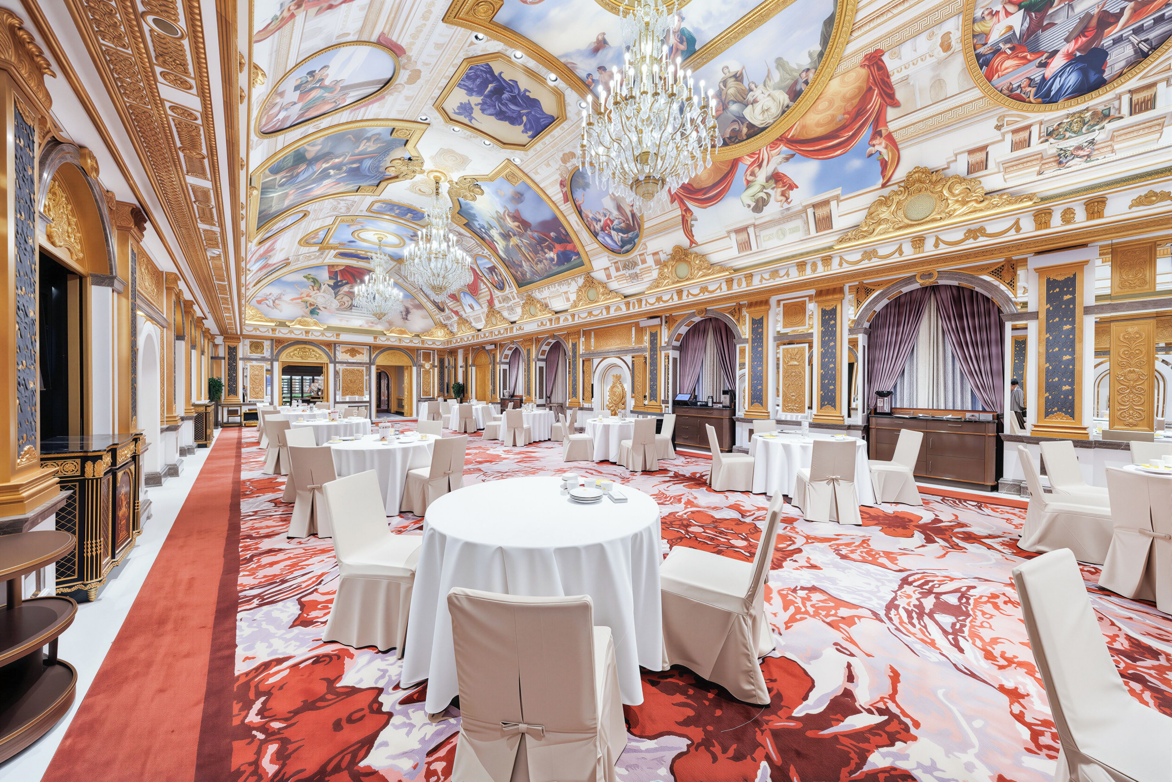 Ein prächtiger Ballsaal mit aufwendigen Deckenfresken, Kristalllüstern und einem roten Teppich.