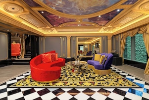 Un lobby lujoso con techo ornamentado, un conjunto de sofá rojo y morado, y una alfombra estampada.