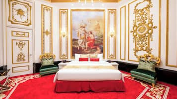A luxurious bedroom with a large bed, ornate gold detailing, and a red carpet.