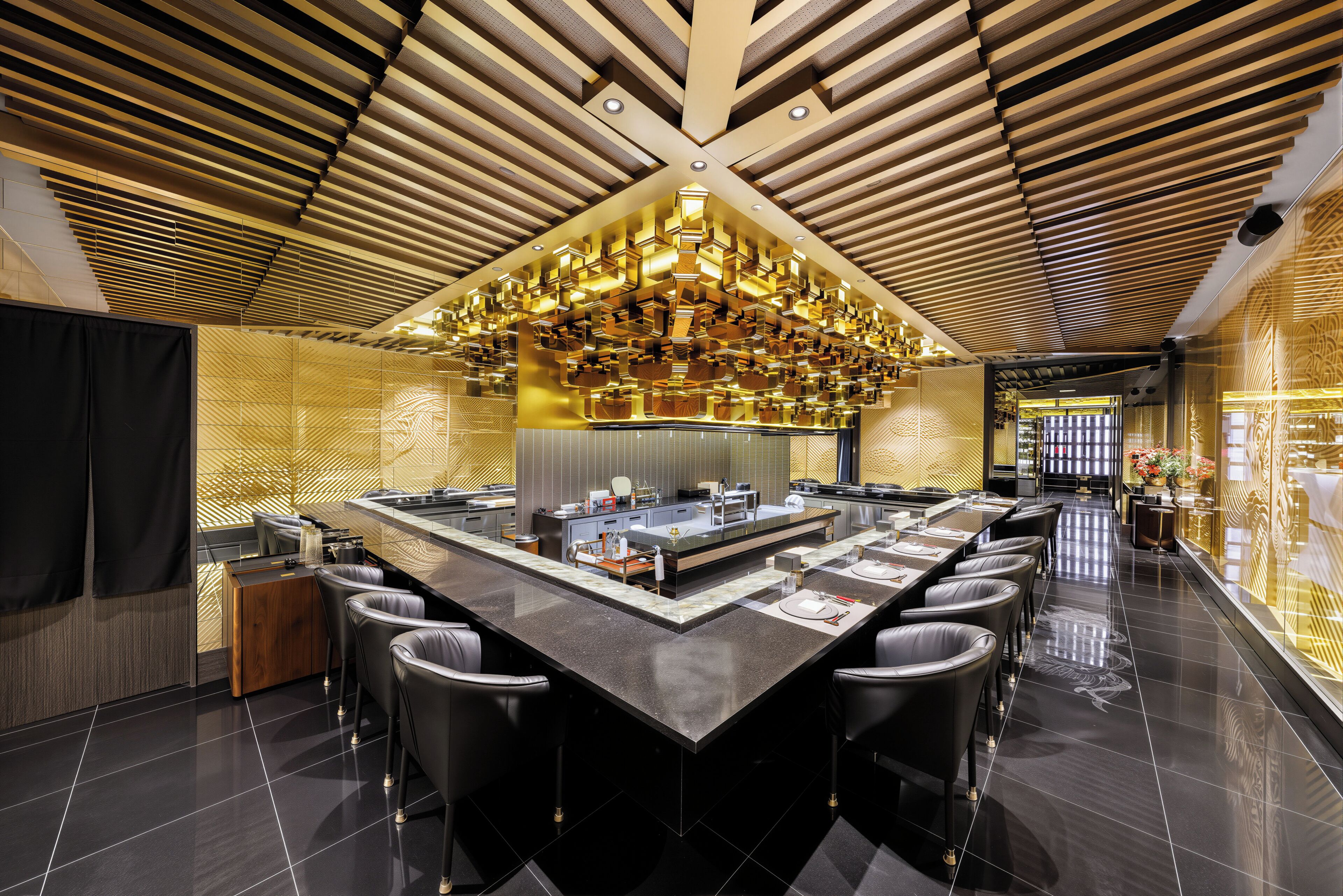 A modern restaurant with a central island, black bar stools, and a ceiling with wooden slats and pendant lighting.