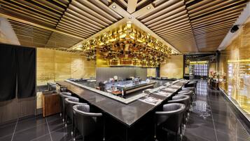 A modern restaurant with a central island, black bar stools, and a ceiling with wooden slats and pendant lighting.