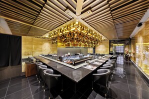 Un restaurante moderno con una isla central, taburetes negros y un techo de listones de madera con iluminación colgante.