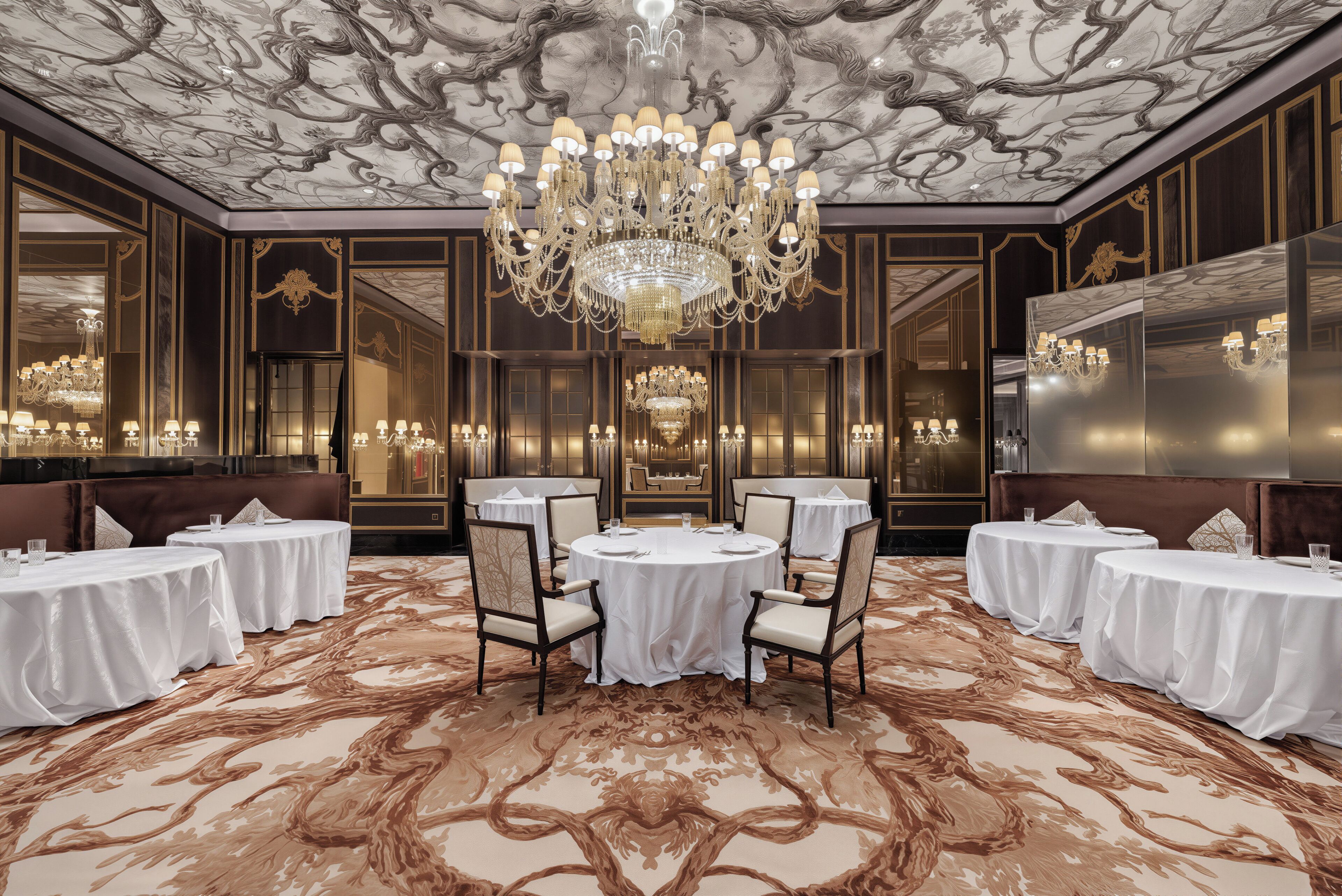 A luxurious hotel room with a large chandelier, round dining table, and multiple seating arrangements.