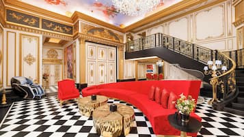 A luxurious lobby with a checkered floor, a red sofa, a massage chair, and a grand staircase.