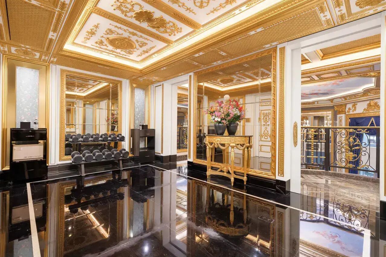 Eine luxuriöse Hotelhalle mit einem hochglanzpolierten Marmorboden, aufwendiger Goldverzierung an der Decke und einem großen Spiegel, der den Raum widerspiegelt.