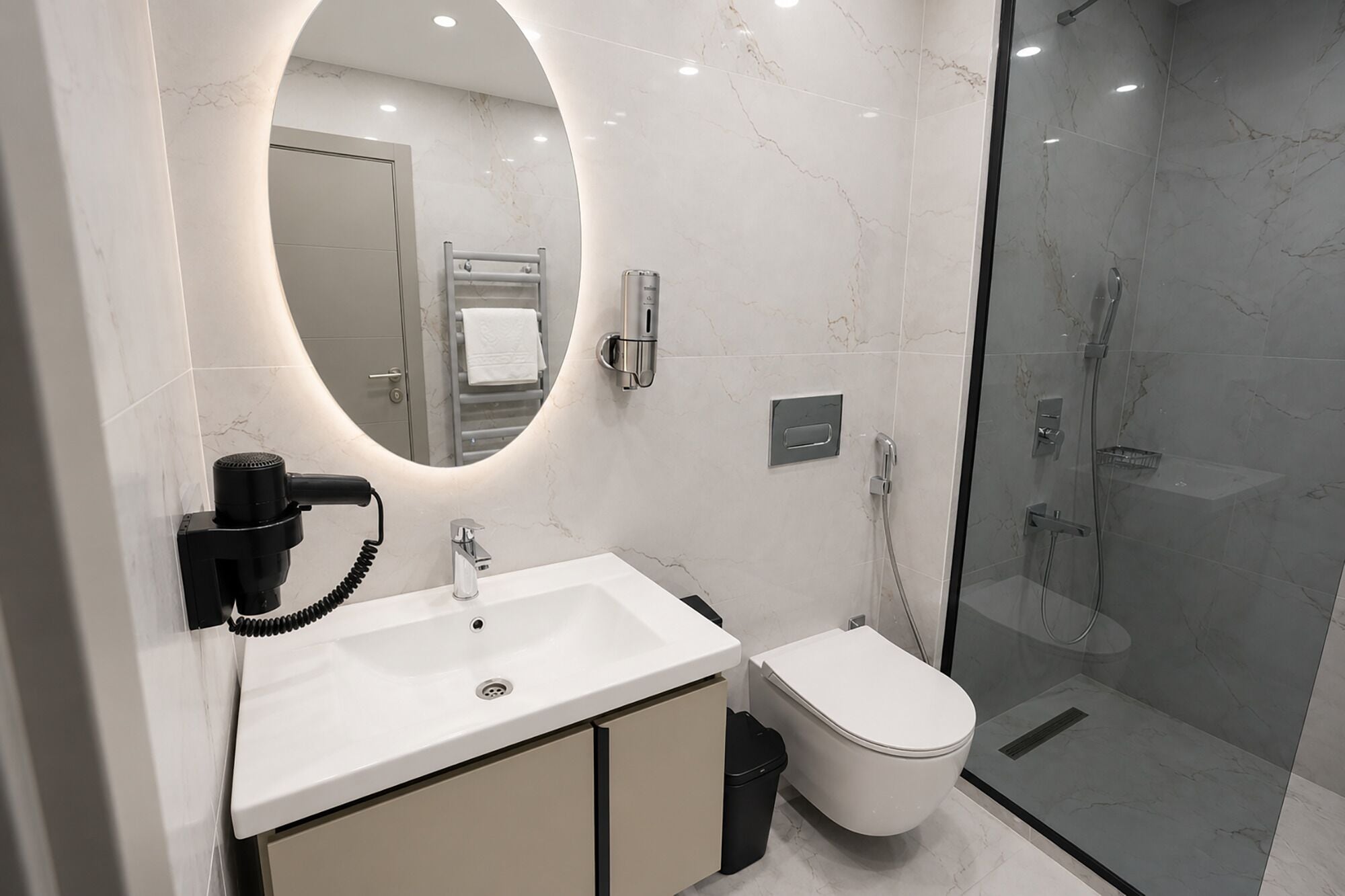 A modern bathroom with a marble sink, a toilet, a glass-enclosed shower, and a built-in mirror.
