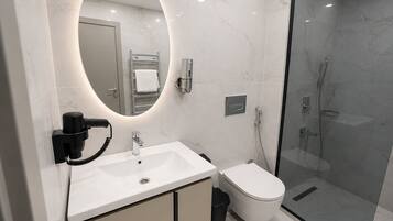 A modern bathroom with a marble sink, a toilet, a glass-enclosed shower, and a built-in mirror.