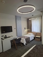 Quarto de hotel moderno com televisão de tela plana, escrivaninha, cadeira, cama e janela com cortinas.