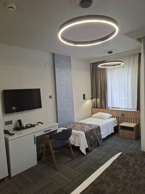 A modern hotel room with a flat-screen TV, a desk, a chair, a bed, and a window with curtains.