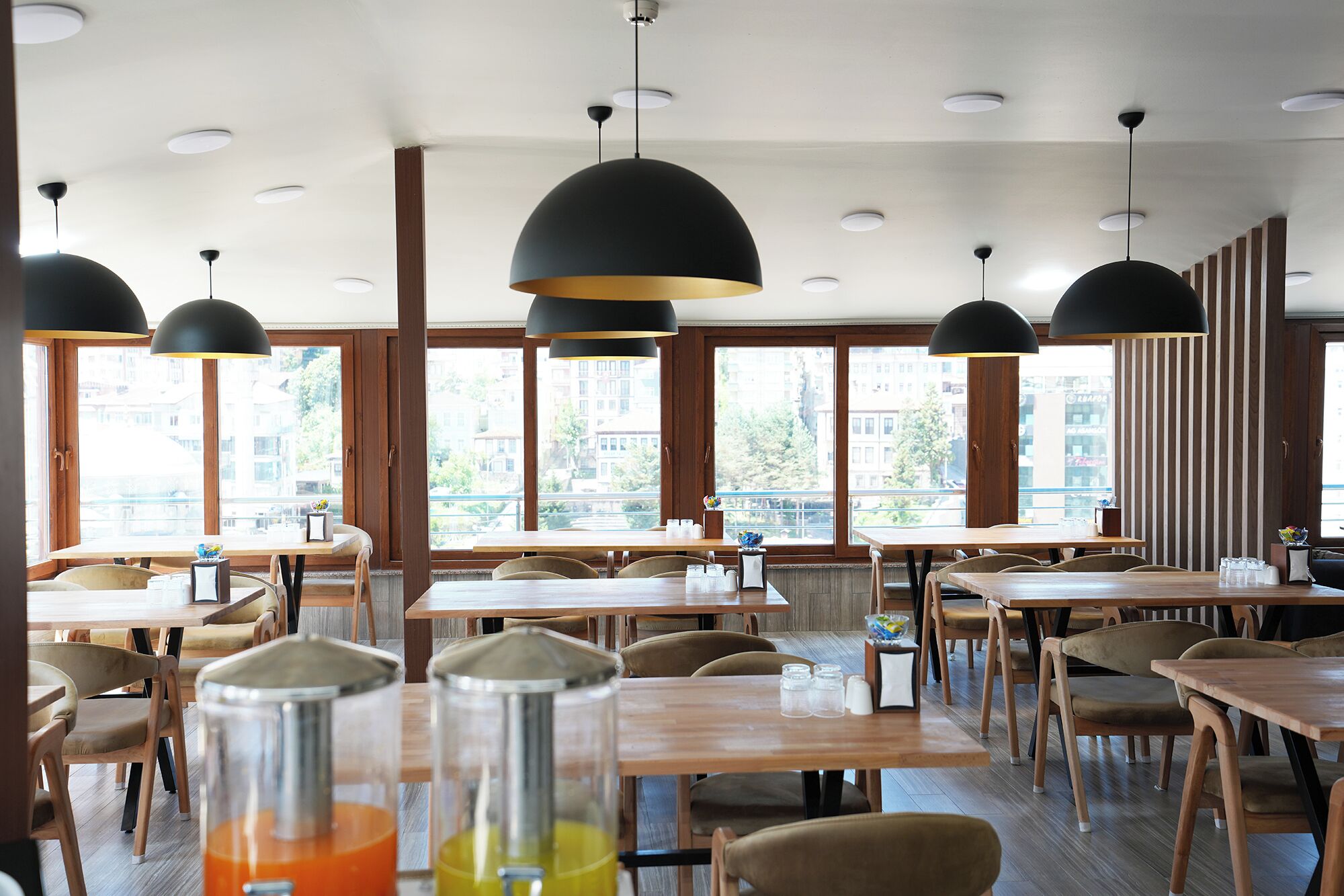 A restaurant interior with multiple tables and chairs, large windows, and pendant lighting.