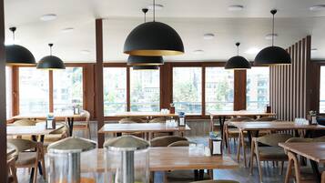 A restaurant interior with multiple tables and chairs, large windows, and pendant lighting.