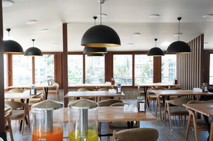 Interior de restaurante con varias mesas y sillas, ventanas amplias e iluminación colgante.