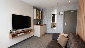 A modern living room with a flat-screen TV, a sofa, a coffee table, and a kitchen area with cabinets and a mirror. - Kaçkar Otel (Rize)