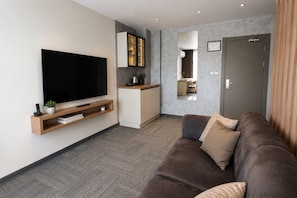 A modern living room with a flat-screen TV, a sofa, a coffee table, and a kitchen area with a countertop and cabinets.