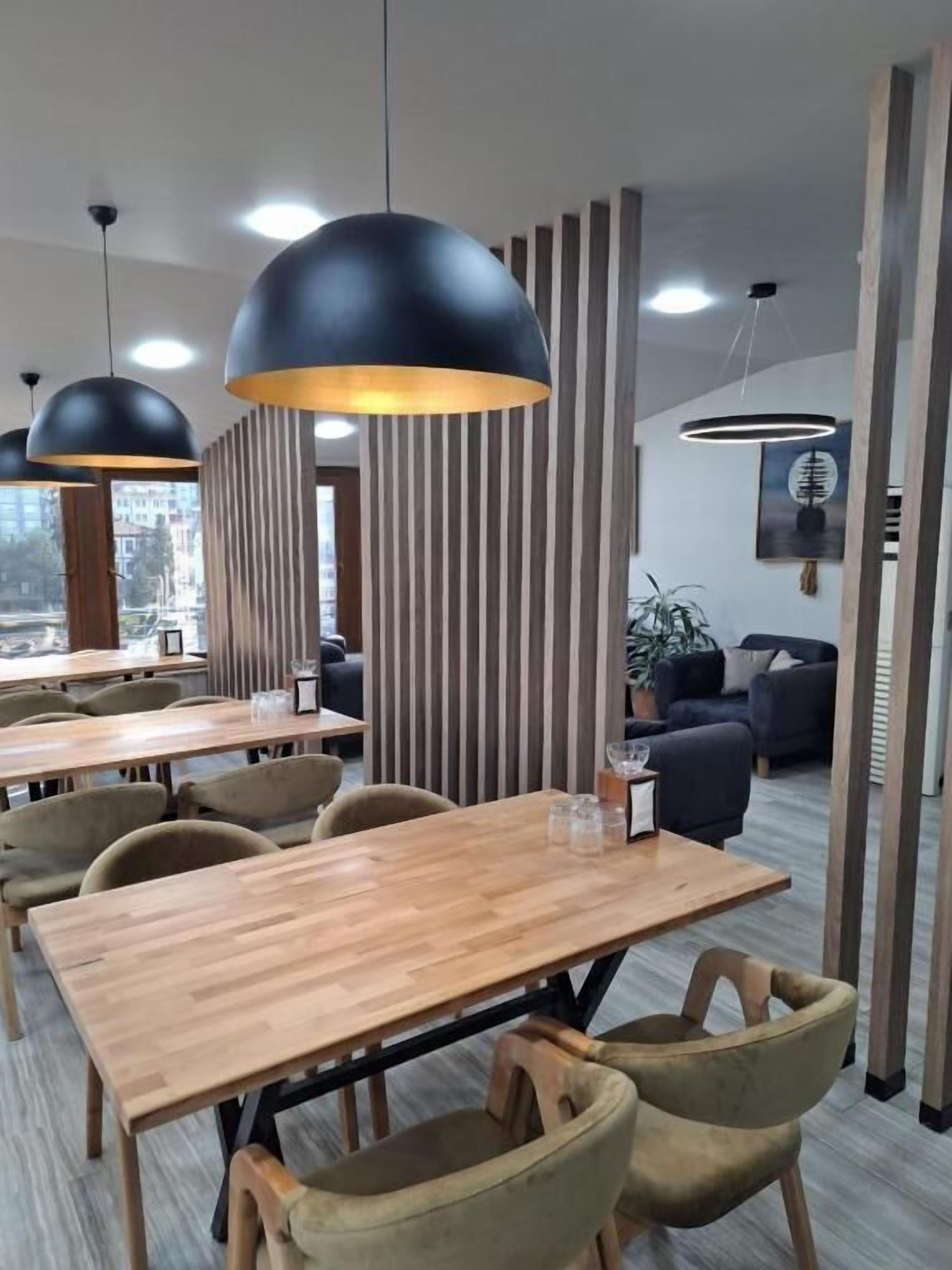 A modern dining area with wooden tables and chairs, black pendant lighting, and vertical wooden slats.