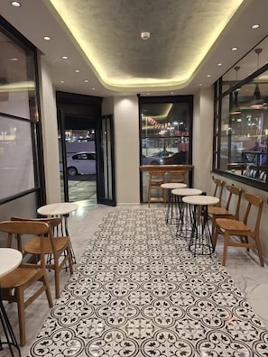 Un pasillo con suelo estampado, sillas y mesas de madera, que conduce a una ventana con vistas al exterior.