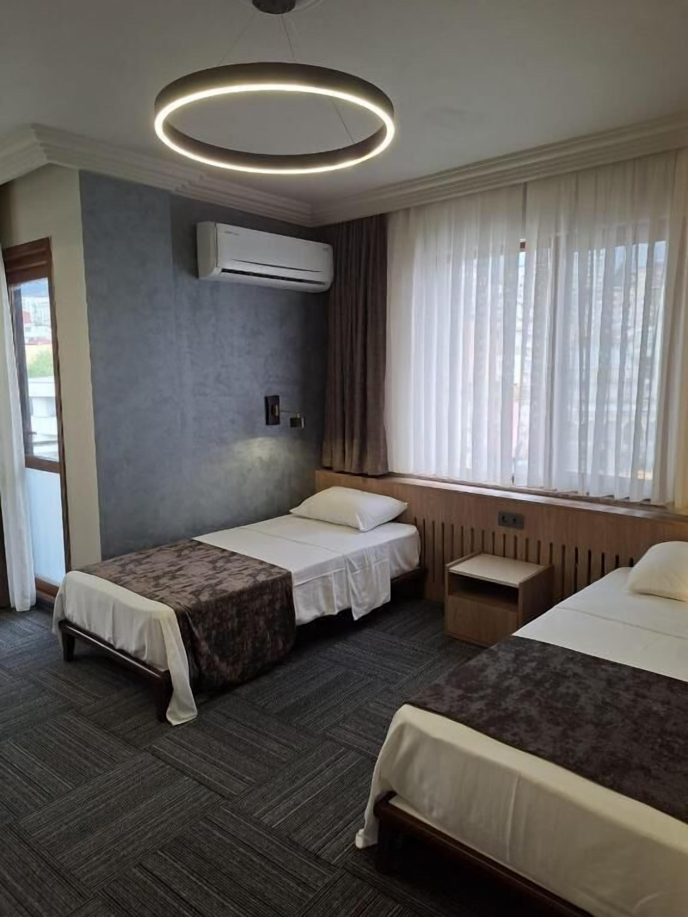 Habitación de hotel con dos camas, una lámpara en el techo, aire acondicionado y una ventana con cortinas.