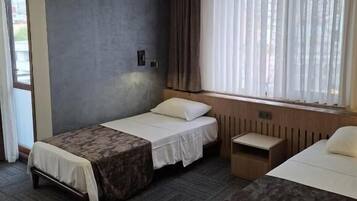 Habitación de hotel con dos camas, una lámpara en el techo, aire acondicionado y una ventana con cortinas.