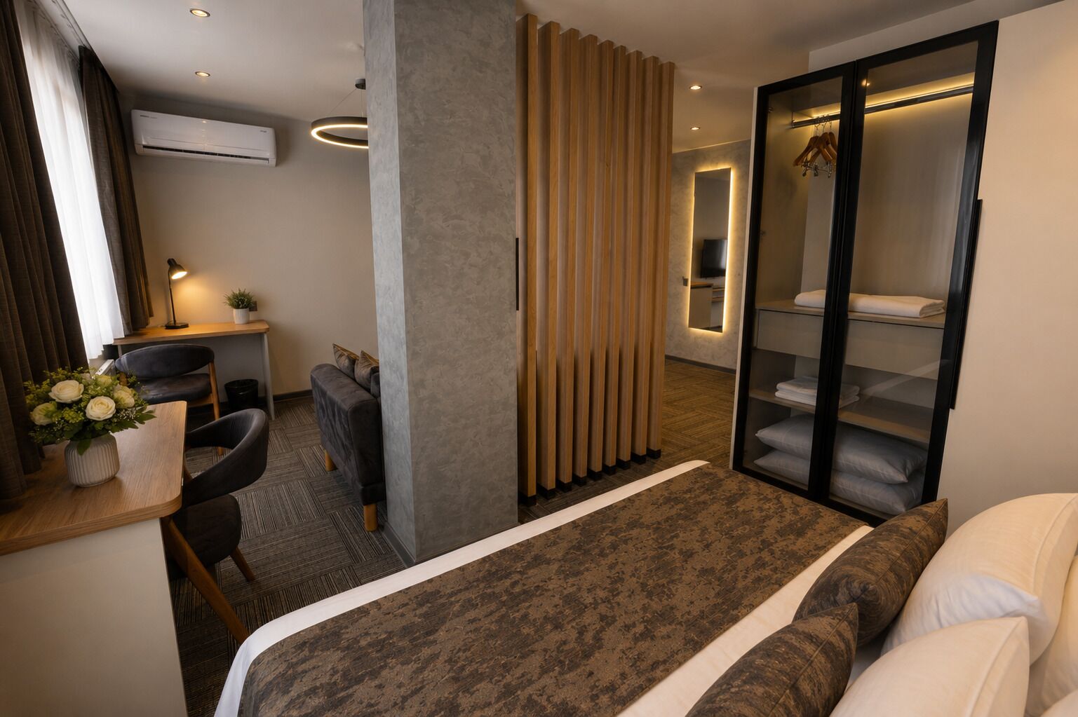 Una habitación de hotel moderna con una cama, un escritorio con una silla, una mesita con un florero y un armario, además de un espejo.