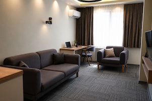 A modern hotel room with a sofa, armchair, desk, and television.