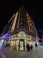 A multi-story hotel with a distinctive corner design, outdoor seating, and illuminated signage.