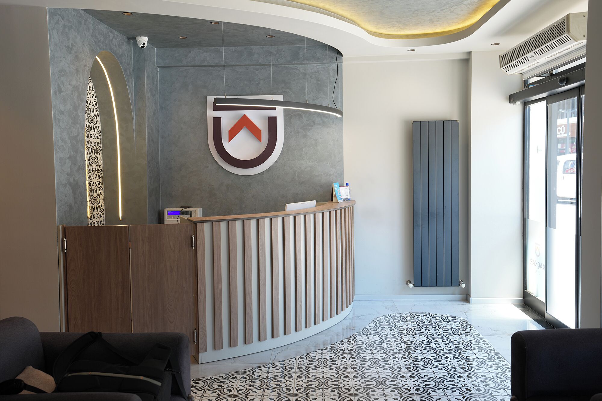 A reception area with a modern design, a logo on the wall, a reception desk, and a patterned floor.