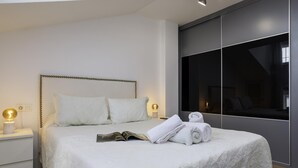 Un dormitorio moderno con una cama grande, lámparas de noche, una mesita de noche y un amplio ventanal.