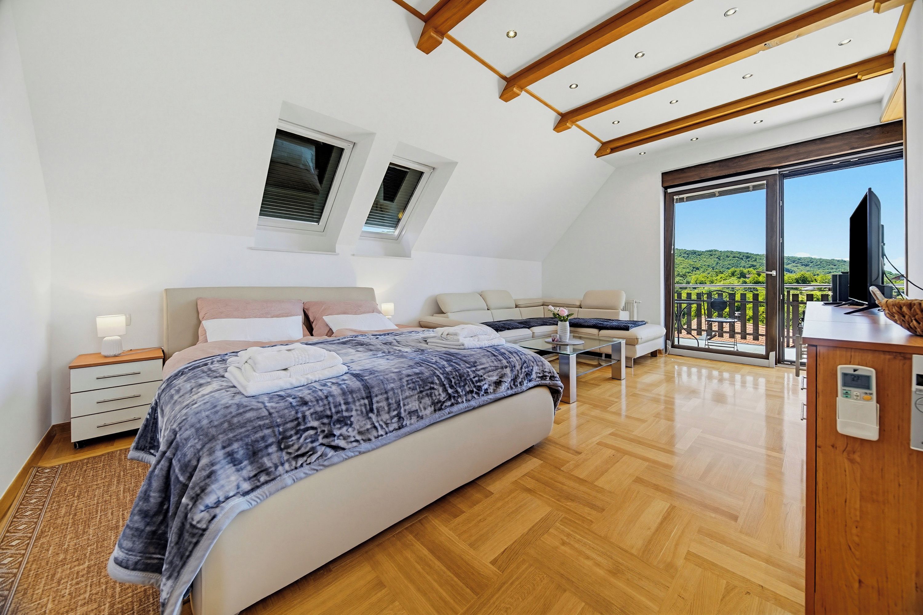 A bedroom with a bed, bedside tables, a sofa, a TV, and a balcony with a view.