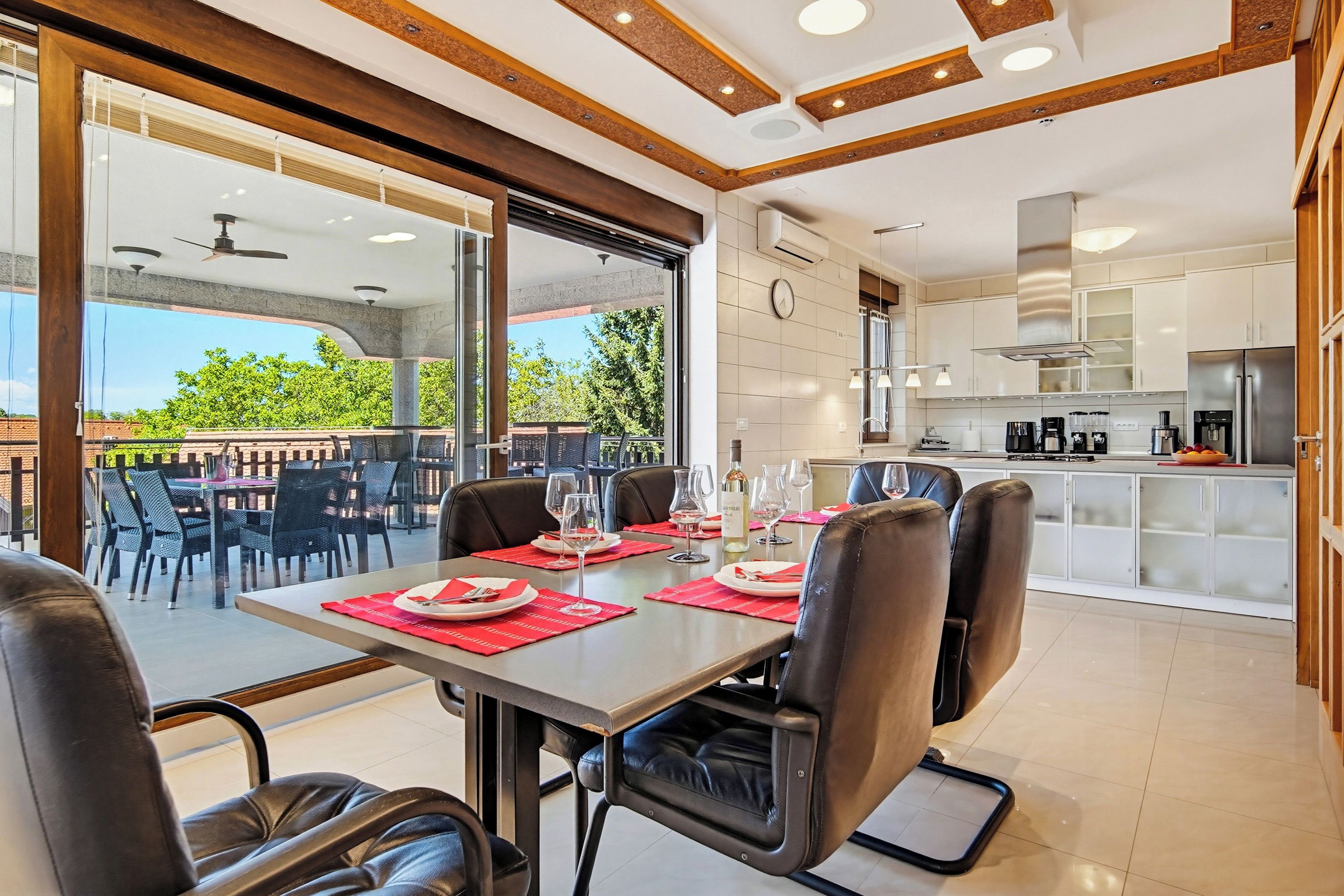 A dining area with a table set for four, a kitchen in the background, and a view of the outdoors.