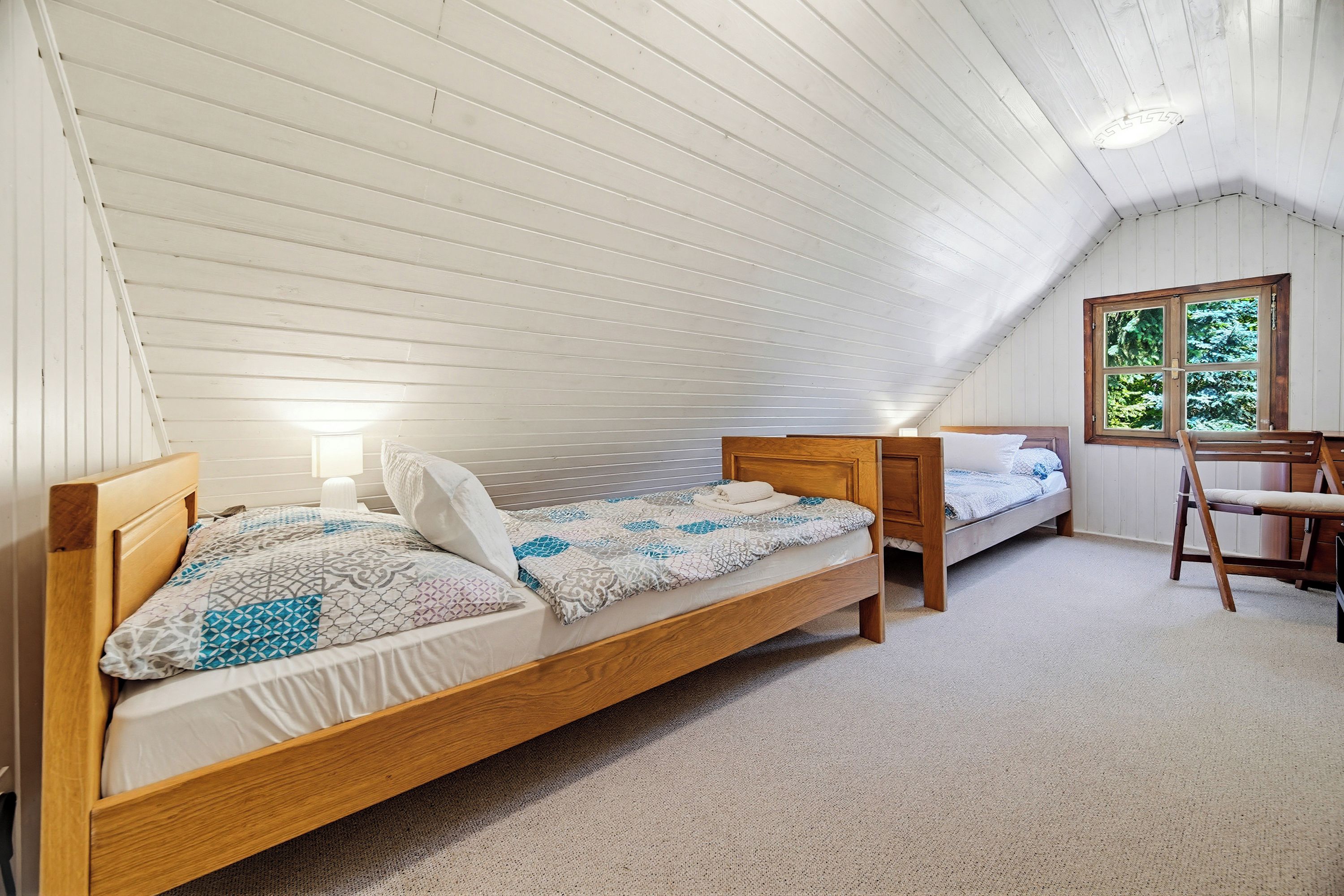 A bedroom with two wooden beds, a window, and a chair.