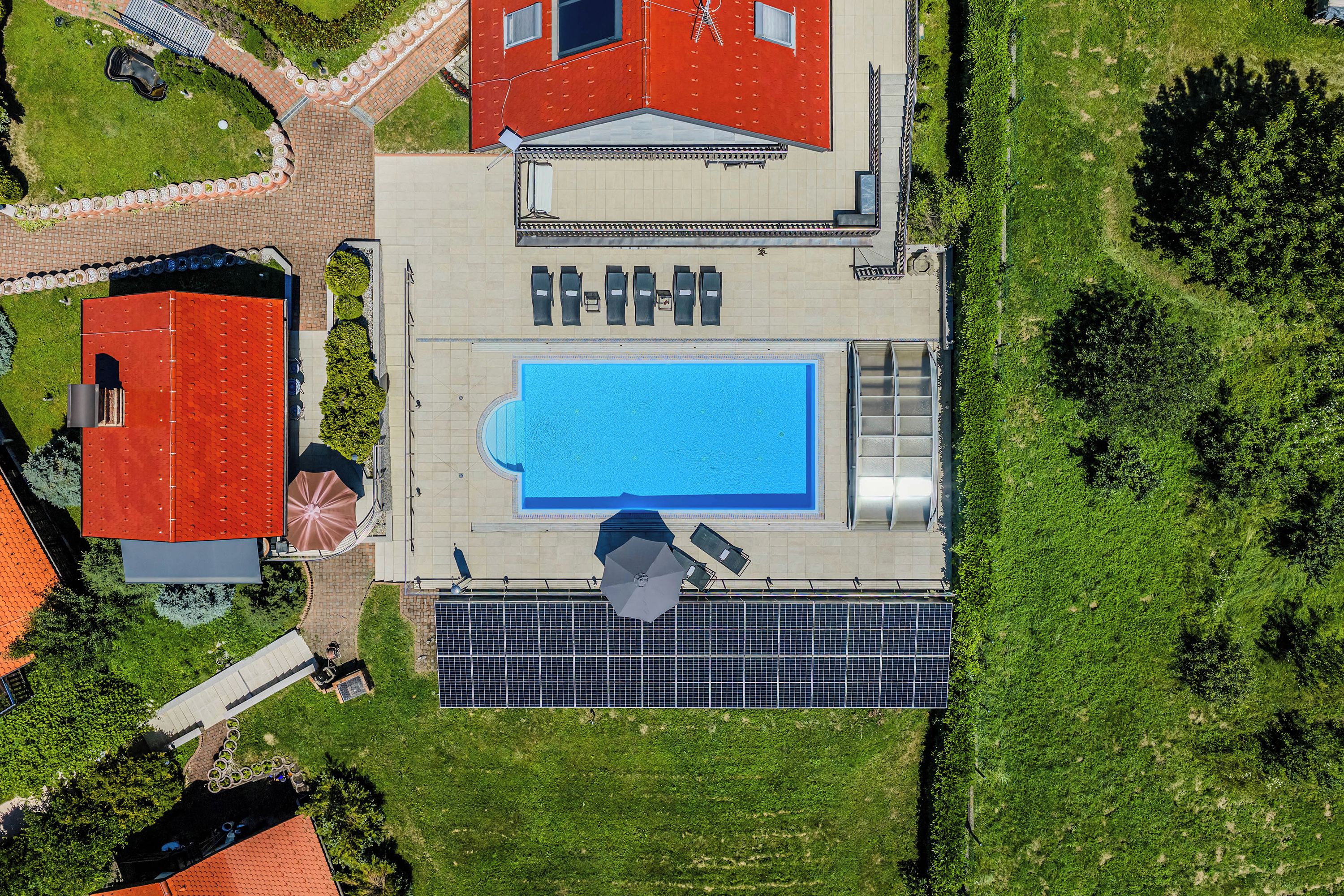 An aerial view of a property with a swimming pool, solar panels, and a red-roofed building.