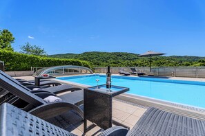 Ein Poolbereich mit Liegestühlen, einem Tisch mit Flasche und Glas sowie Blick auf einen Berg.