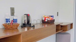 A clean, modern kitchenette with a wooden countertop, a kettle, a basket of bottled water, and a bag of snacks.