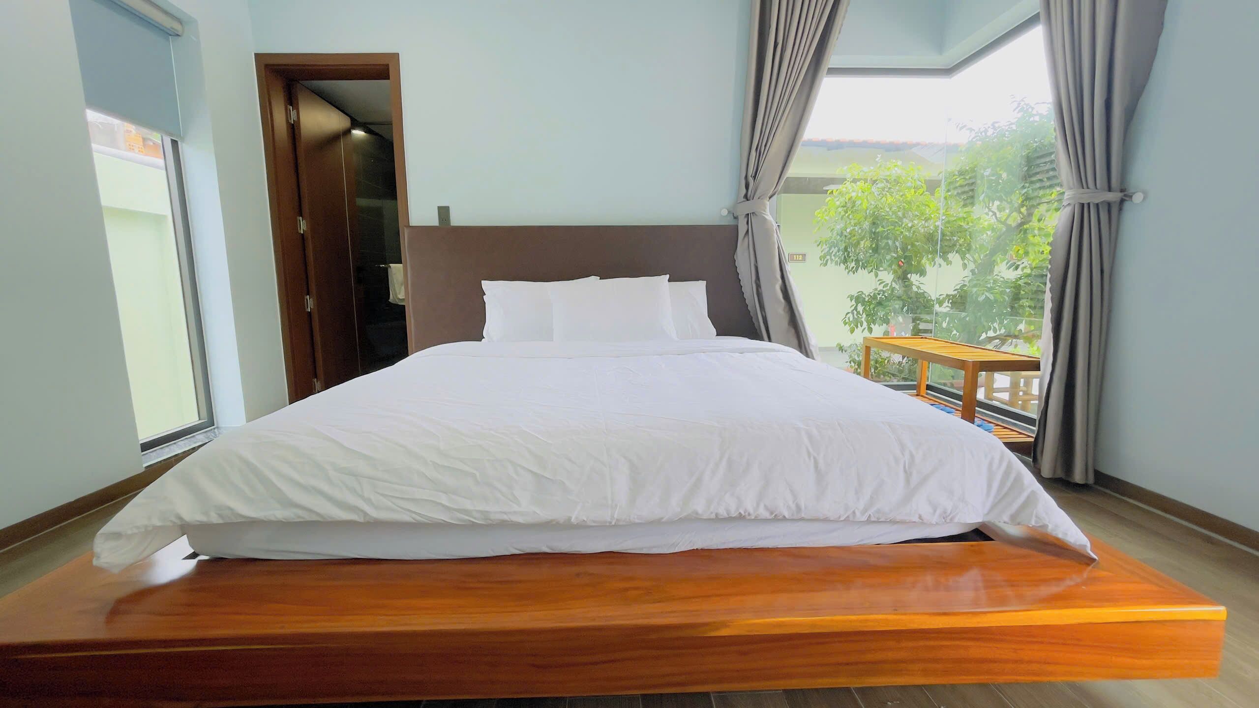 Une chambre moderne avec un lit surélevé en bois, une vue sur la verdure et une petite table en bois.