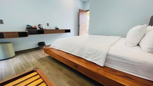 A modern bedroom with a wooden bed, a small bedside table, a wall-mounted shelf with toiletries, and a window with natural light.