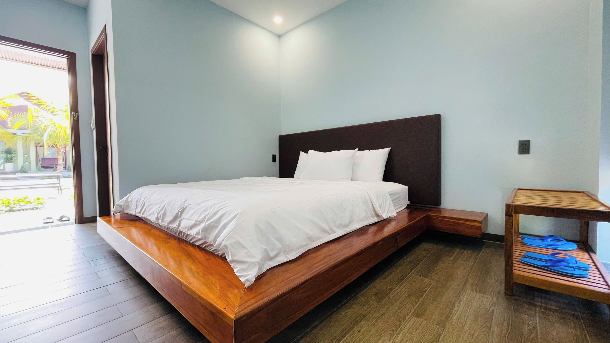 A modern bedroom with a wooden bed, a nightstand, and a small wooden table with blue flip-flops.