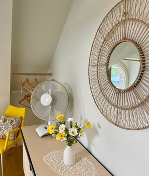 A room with a fan, a mirror, a chair, a table with a vase of flowers, and a wooden hanger rack. - AppartCosy 20 Country House Near “Régalante” (Landavran)