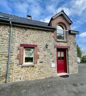 A stone building with a red door, a small window, and a balcony with a metal railing. - AppartCosy 20 Country House Near “Régalante” (Landavran)