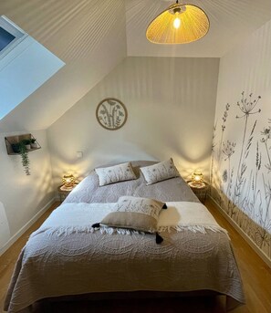 A bedroom with a bed, two bedside tables, a wall-mounted light fixture, a window, and a wall with a floral pattern. - AppartCosy 20 Country House Near “Régalante” (Landavran)
