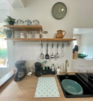 A kitchen with a clock, shelves with jars, utensils, a coffee maker, and a sink. - AppartCosy 20 Country House Near “Régalante” (Landavran)