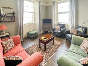 A living room with a sofa, armchairs, a coffee table, a television, and a bookshelf. - Pier View is a seafront property with amazing views and dramatic sunsets. (Pier View)